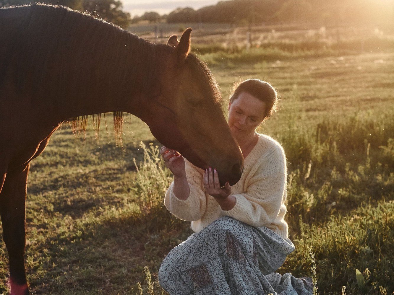 Kathrin Keiper kniet bei ihrem Pferd in der Abendsonne